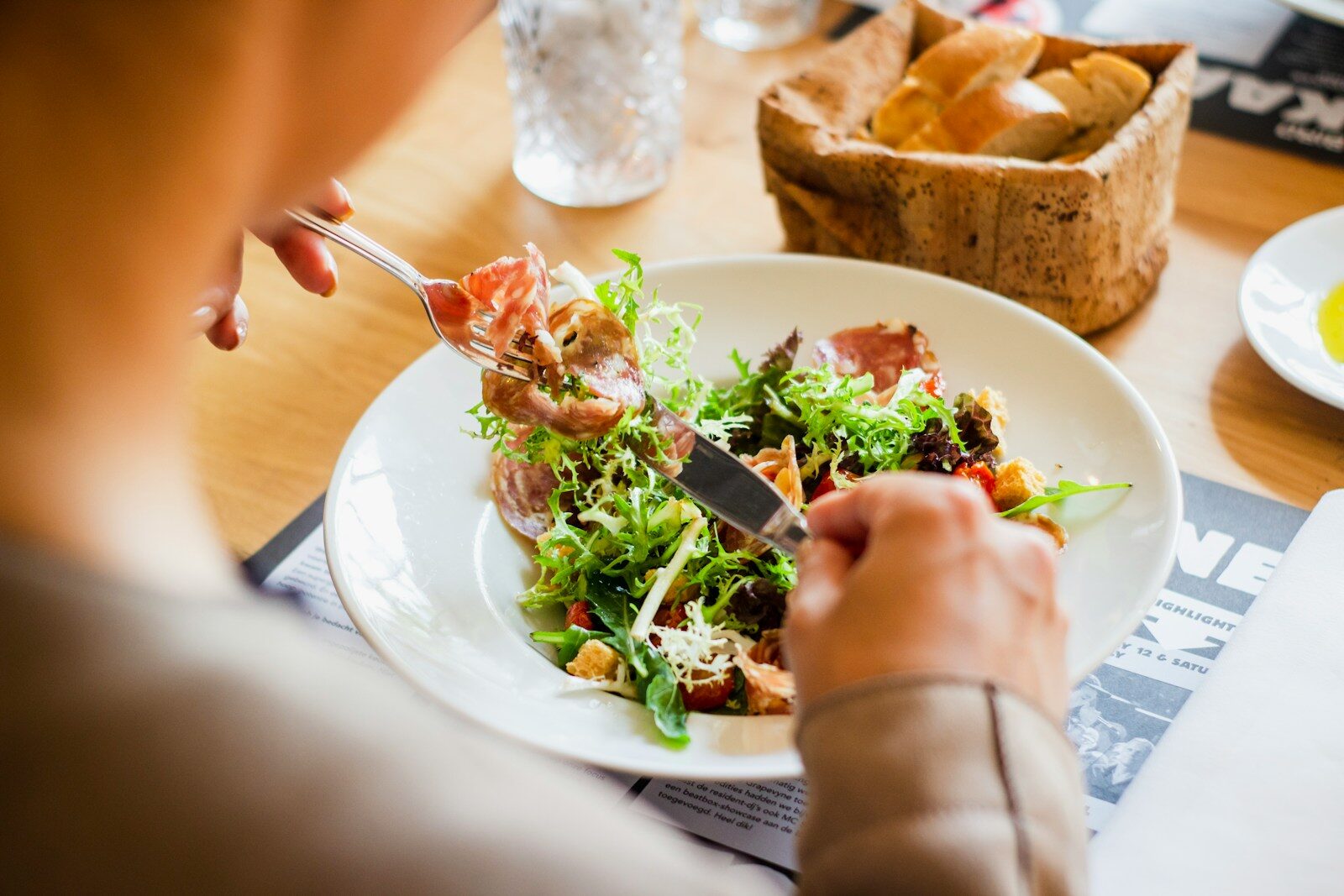 A person eating a salad with cured meat and croutons from a white plate